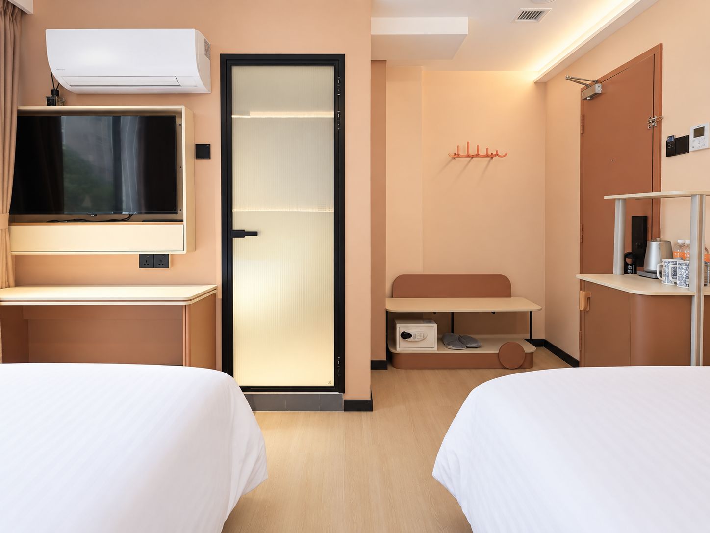 Une chambre d’hôtel avec deux lits, une télévision, une armoire, un bureau et un meuble pour ranger les chaussures.