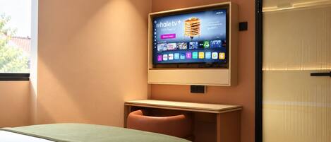 A hotel room with a bed, a desk, a TV mounted on the wall, and an air conditioning unit.