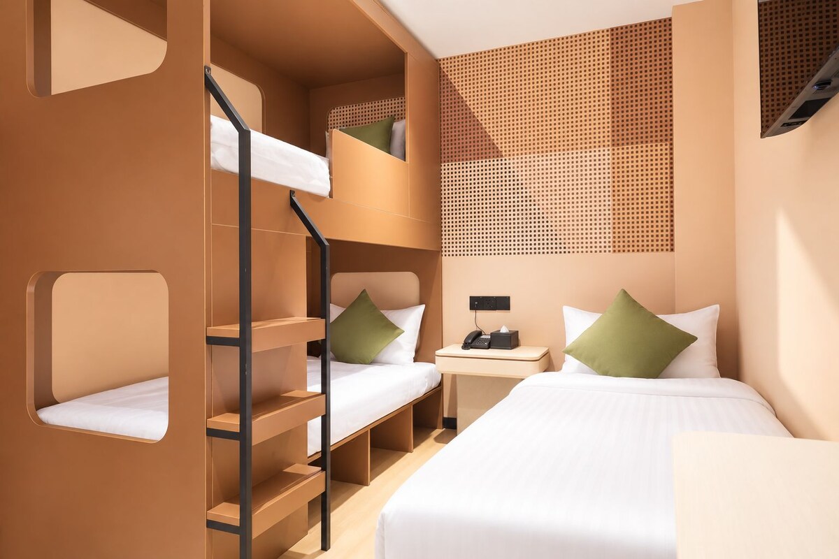 Habitación de hotel con literas, una mesita de noche con teléfono y pañuelos, y una pared con diseño perforado.