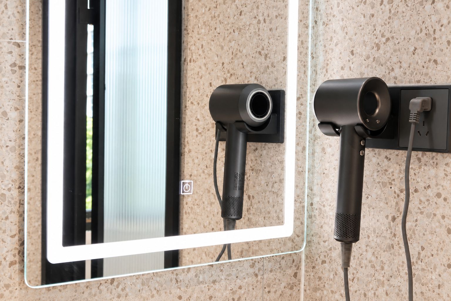Secador de pared y dispositivo enchufable, ambos con cables de alimentación, frente a una pared de azulejos con vetas.