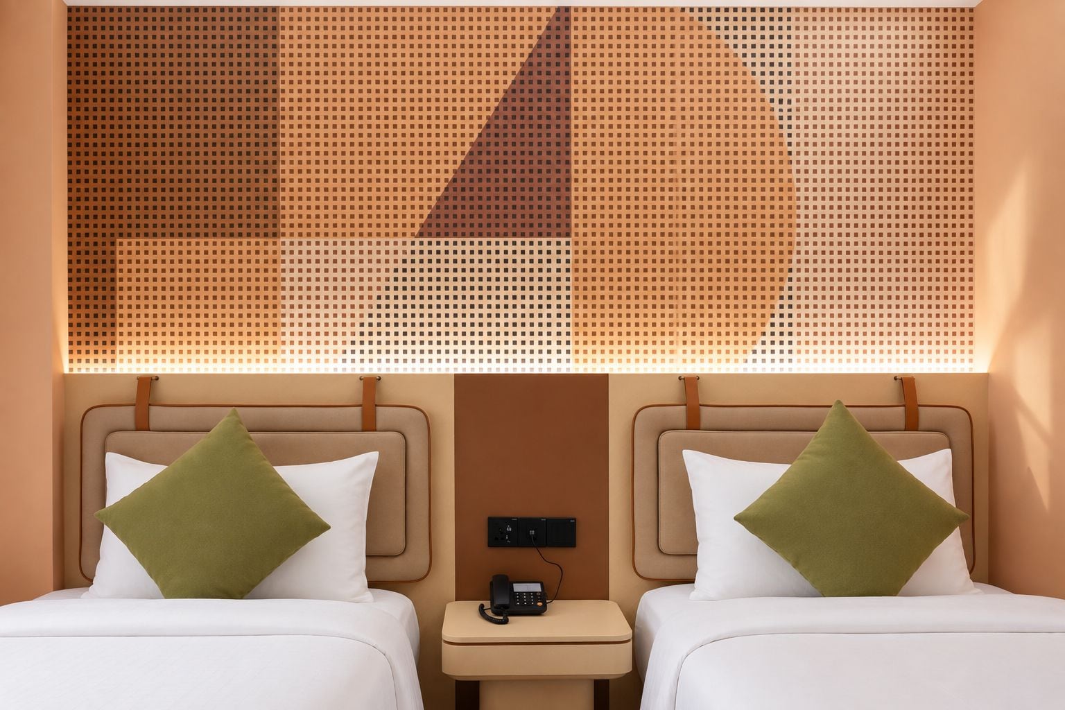 A hotel room with two beds, each with a pillow, a small bedside table with a phone, and a wall-mounted light fixture.