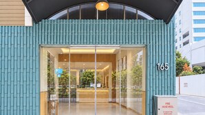Entrada moderna de un edificio con puerta de vidrio, un carrete de manguera contra incendios y el número '165' en la pared.