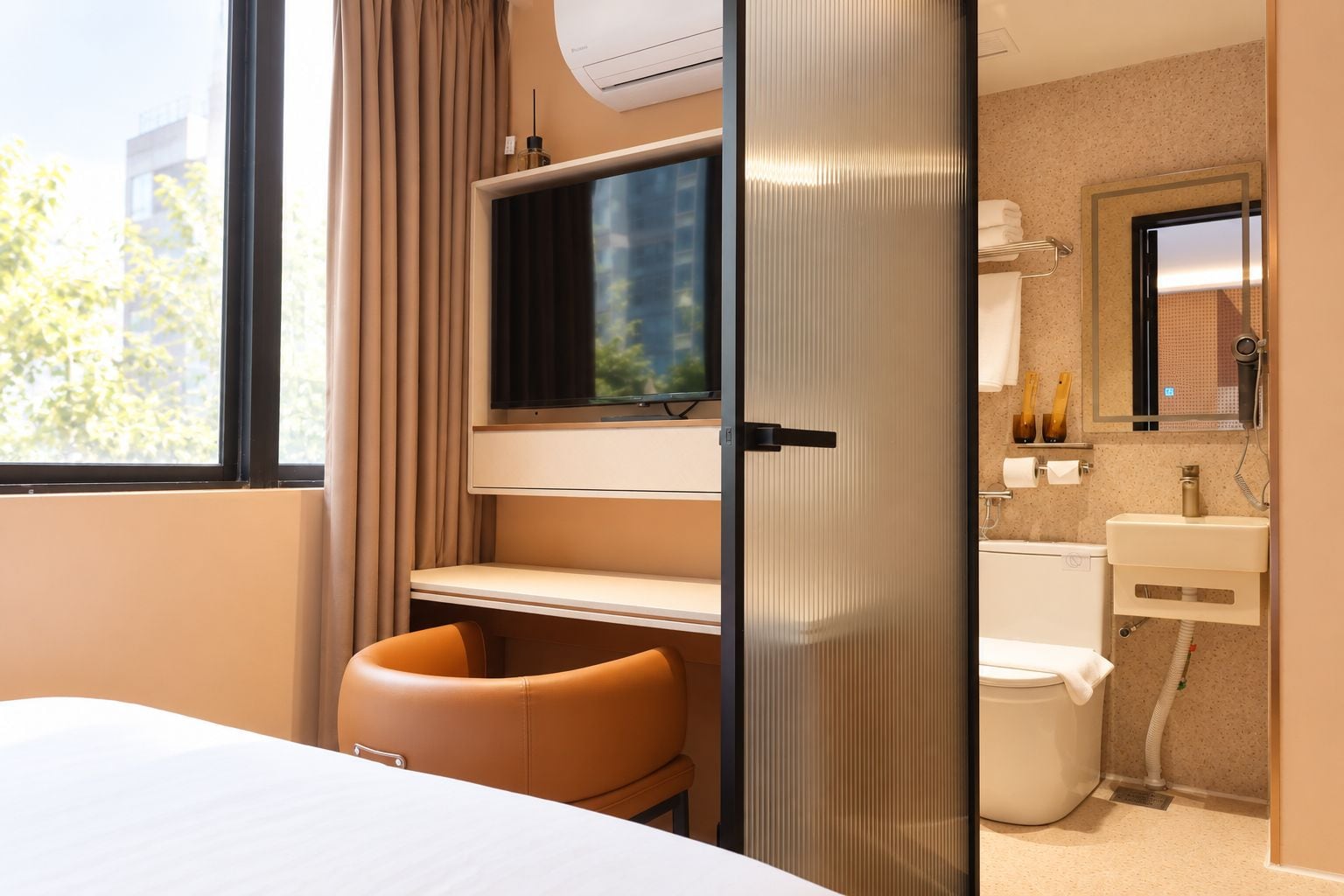 Ein Hotelzimmer mit einem Bett, einem Schreibtisch mit Flachbildfernseher, einem Stuhl, einem Badezimmer mit Waschbecken und Toilette sowie einem Fenster mit Vorhängen.