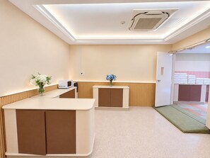 Una zona de recepción con mostrador, microondas y una pequeña mesa con flores.