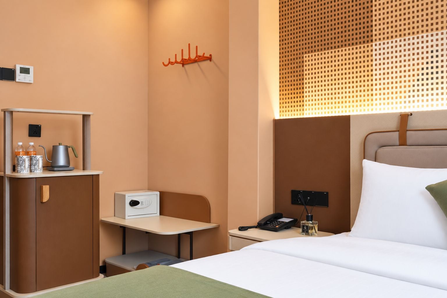 Habitación de hotel con cama, escritorio, silla, teléfono y una mesita con tetera y botellas.