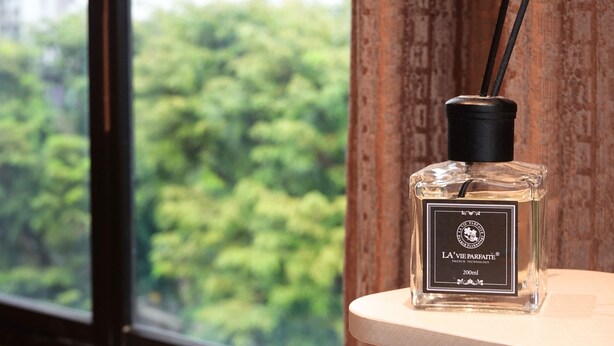 A bottle of La Vie Parfaite perfume on a wooden surface near a window with a view of trees. - A Hotel Farrer Park - Newly Renovated (Singapore)