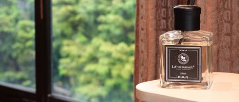A bottle of La Vie Parfaite perfume on a wooden surface near a window with a view of trees.