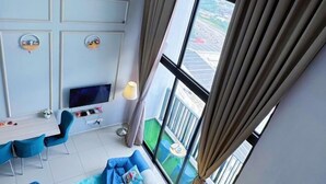 Una sala de estar moderna con una televisión de pantalla plana, sillas azules, un sofá y un balcón con vistas a la ciudad.