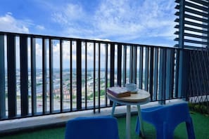 A balcony with a view of a cityscape, a small round table with a book and a cup, and two blue chairs. - Doraemon @ Hyde Towel Duplex Fully AiCON 2BR (Shah Alam)