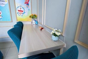 A dining area with a wooden table, teal upholstered chairs, a vase with flowers, and cartoon character posters on the wall.