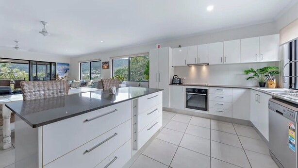 Una cocina moderna con armarios blancos, una isla central y vistas al exterior.