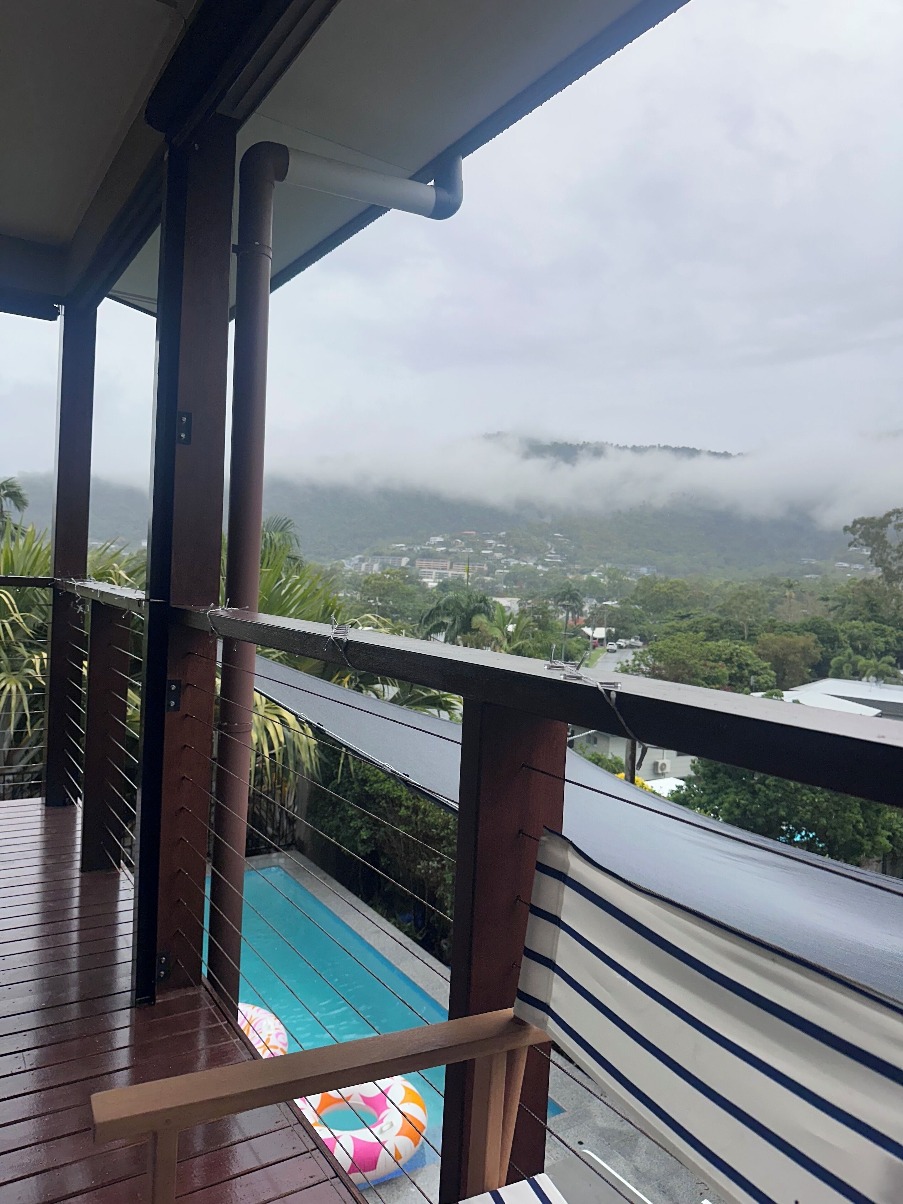 Une terrasse en bois offrant une vue sur une piscine et sur une ville située au loin.