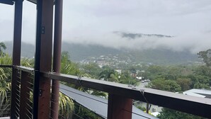 Una terraza de madera con vista a una piscina y un pueblo lejano.