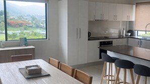 Una cocina moderna con armarios blancos, una mesa de comedor con sillas y vistas a un paisaje a través de un amplio ventanal.