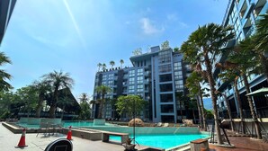 A modern hotel with a large pool area, surrounded by palm trees and a multi-story building in the background. - 1BR with Rooftop Pool & Gym  C191 (Kamala)