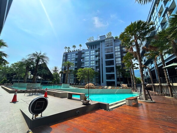 Un hotel moderno con una vasta area piscina, circondata da palme e un edificio a più piani sullo sfondo.
