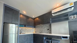 A modern kitchen with a stainless steel refrigerator, dark wood cabinets, a tiled backsplash, and a built-in stove. - 1BR with Rooftop Pool & Gym  C191 (Kamala)