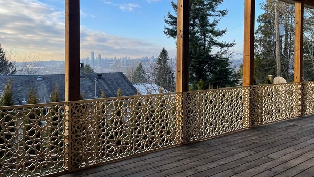 Un espace extérieur abrité offrant une vue sur les toits d’une ville, avec des piliers en bois et une clôture décorative.