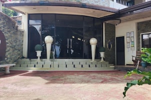 Fachada de edificio con techo curvo, puertas de cristal amplias y pared de piedra.