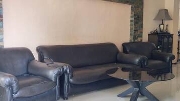 Una sala de estar con un sofá de cuero negro, una mesa de centro de vidrio y una lámpara sobre un aparador.
