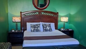 Un lit bien fait, agrémenté d’oreillers à motifs, d’une tête de lit en bois, de deux lampes de chevet et d’un miroir au mur.