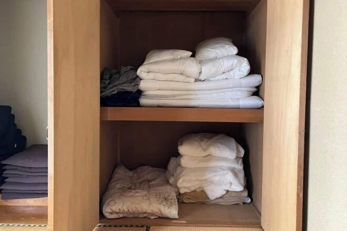 A wooden wardrobe with two shelves, each containing folded blankets and pillows.