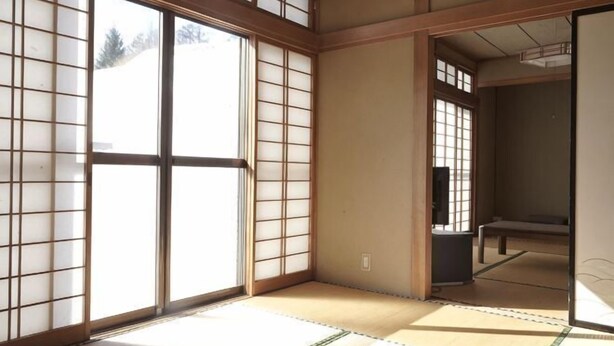 A traditional Japanese room with tatami flooring, sliding doors, and a view through the windows. - Fuse Hot Spring Stay East (Saku)