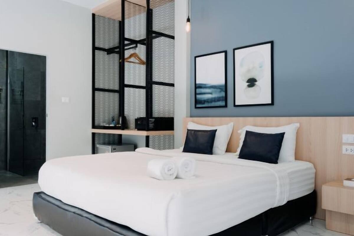 A modern hotel room with a large bed, a wooden headboard, a black metal partition, and two framed pictures on the wall.