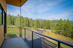 Ein Balkon mit Blick auf eine gebirgige Landschaft, eine gepflasterte Fläche und einen Wald.