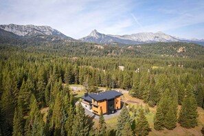 Une maison moderne à deux étages, entourée d’une forêt dense et de montagnes.