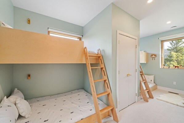 Une chambre avec des lits superposés, une échelle, une porte et une fenêtre donnant sur un beau paysage.