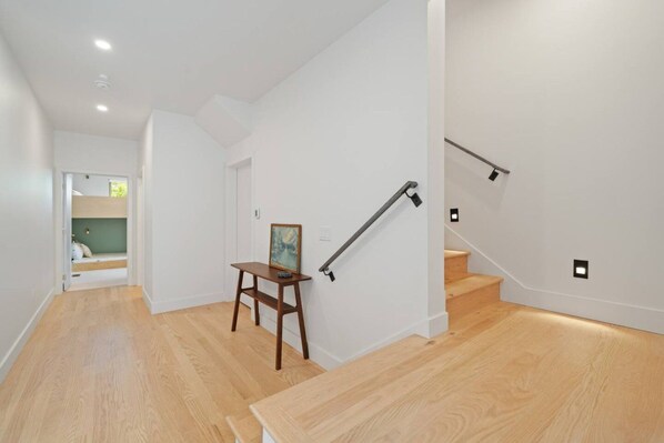 Un intérieur moderne avec un plancher en bois, un escalier doté d’une rampe et une petite table sur laquelle est posée une image.
