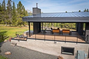 Une terrasse extérieure moderne, dotée d’un espace salon et d’une cheminée, et entourée d’un paysage naturel.