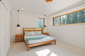 Ein Schlafzimmer mit einem Holzbett, zwei Nachttischen, einem großen Fenster mit Blick auf einen Wald und einer Hängeleuchte.