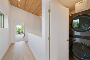 Une buanderie équipée de deux machines à laver et d’une porte donnant sur un balcon avec vue sur les arbres.