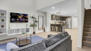 A modern living room with a grey sofa, a coffee table, and a TV mounted on the wall. There is a kitchen area with a refrigerator, microwave, and bar stools. - Cozy 1-bedroom loft ~ Playhouse Square ~ Fitness, BBQ, Fire pit, business center (Cleveland)
