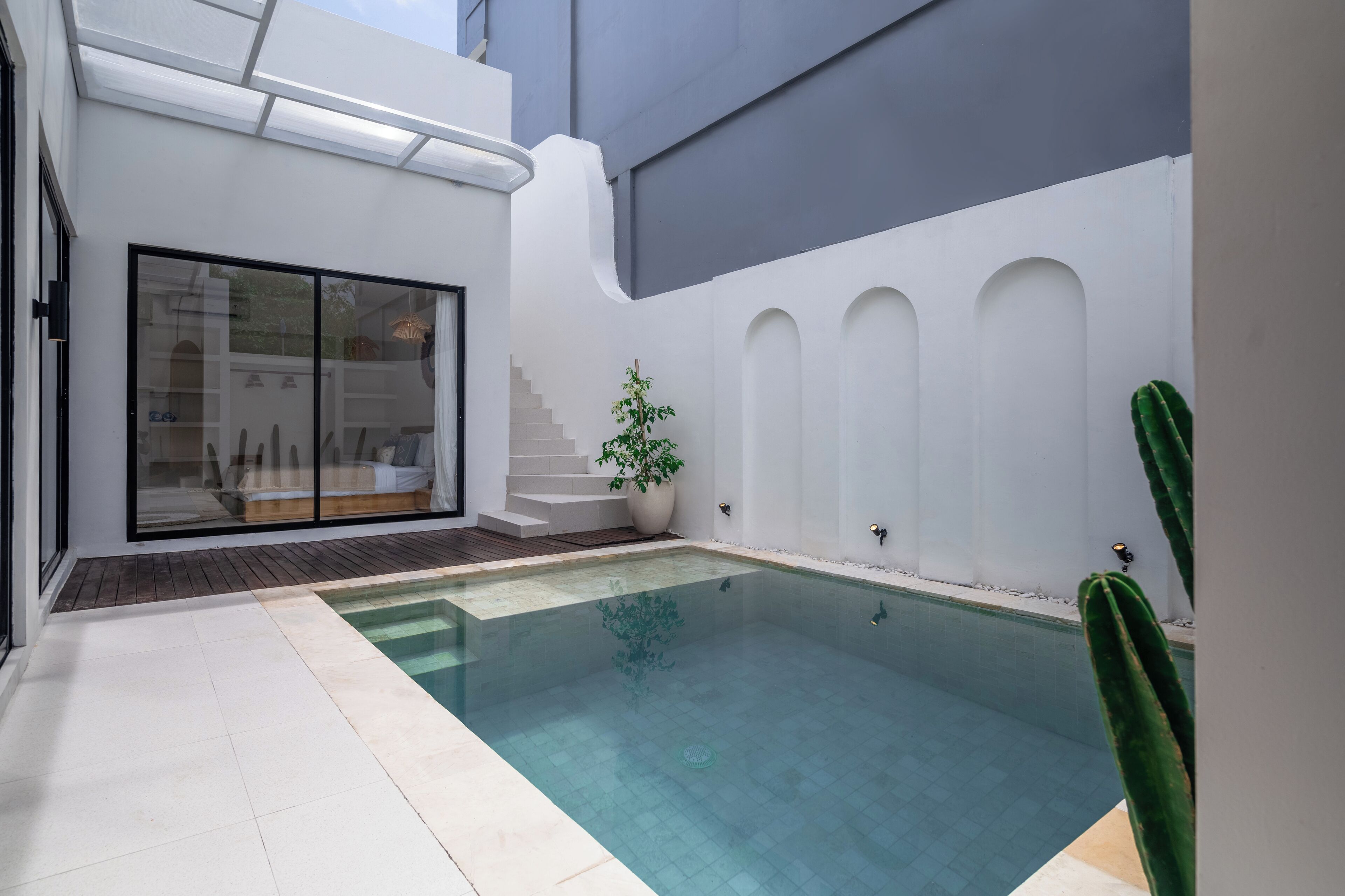 A modern outdoor pool area with a glass door leading to a patio, a small staircase, and a cactus plant.