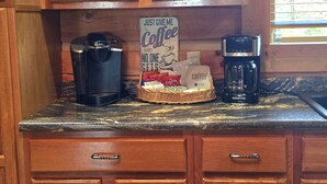 Uma bancada de cozinha com uma cafeteira, um cesto de cápsulas de café e um aviso que diz 'Só me deem o café e ninguém se importa'.
