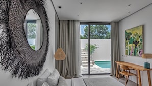 A bedroom with a large bed, a desk, a hanging light, and a view of a swimming pool. - New Magnificent 3BR 5min to Finns & Berawa Beach Villa Alemar (Bali)
