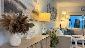 A modern living room with a wooden cabinet, a potted plant, a sofa, and a painting on the wall. - Cozy 1-bedroom condo across street from beach in terrific North Redington Beach (North Redington Beach)