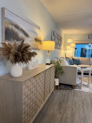 A modern living room with a wooden cabinet, a potted plant, a sofa, and a painting on the wall. - Cozy 1-bedroom condo across street from beach in terrific North Redington Beach (North Redington Beach)