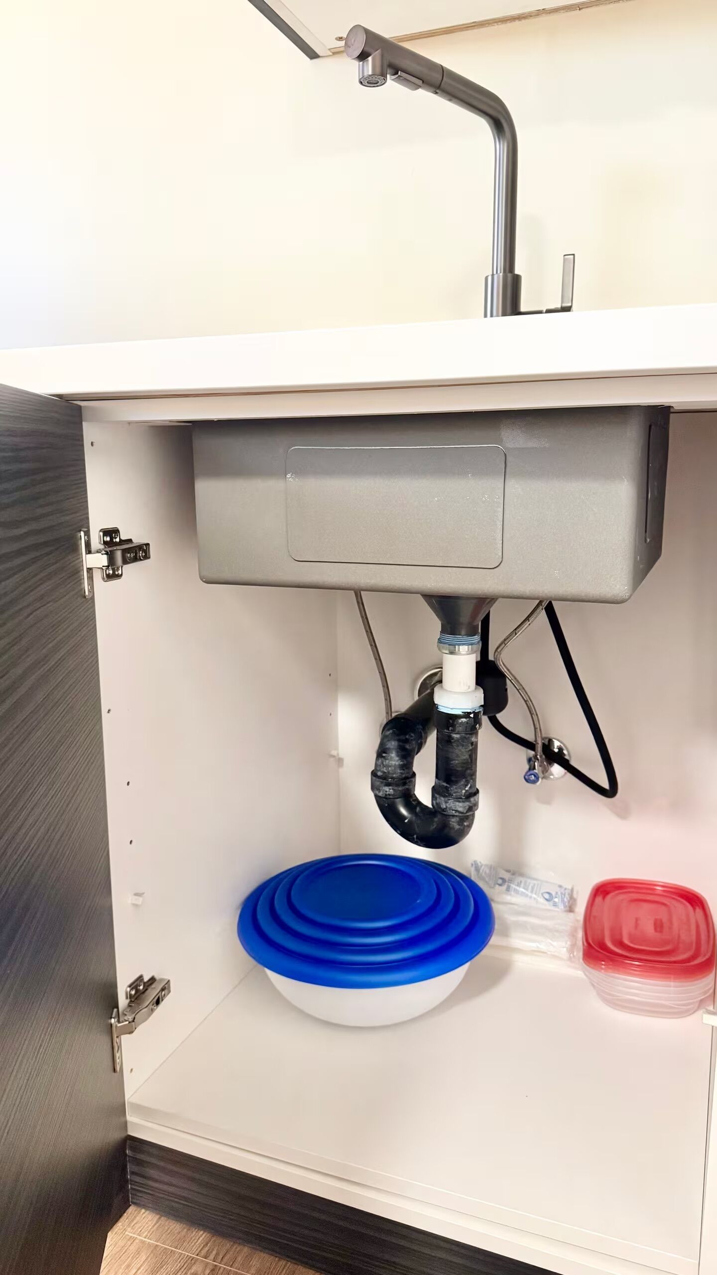Un lavamanos con un gabinete gris, un recipiente para agua azul y un recipiente para agua rojo.