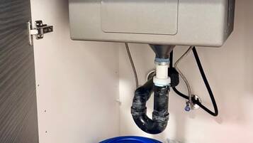 Un lavamanos con un gabinete gris, un recipiente para agua azul y un recipiente para agua rojo.