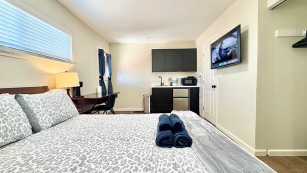 A hotel room with a bed, a desk, a chair, a TV, and a microwave. - Remodeled Spanish Bungalow Suite • Short Walk to SJSU + Parking (San Jose)