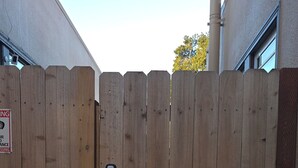 A wooden gate with a keypad lock, a sign indicating no trespassing, and a building with a chimney in the background. - Remodeled Spanish Bungalow Suite • Short Walk to SJSU + Parking (San Jose)