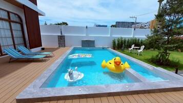 Un área de piscina con jacuzzi, sillas de descanso y un pato inflable amarillo.