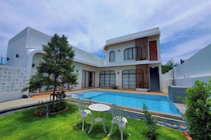 A modern two-story house with a swimming pool, a lawn, and outdoor seating. - Villa NaRa Chaam (Cha-am)