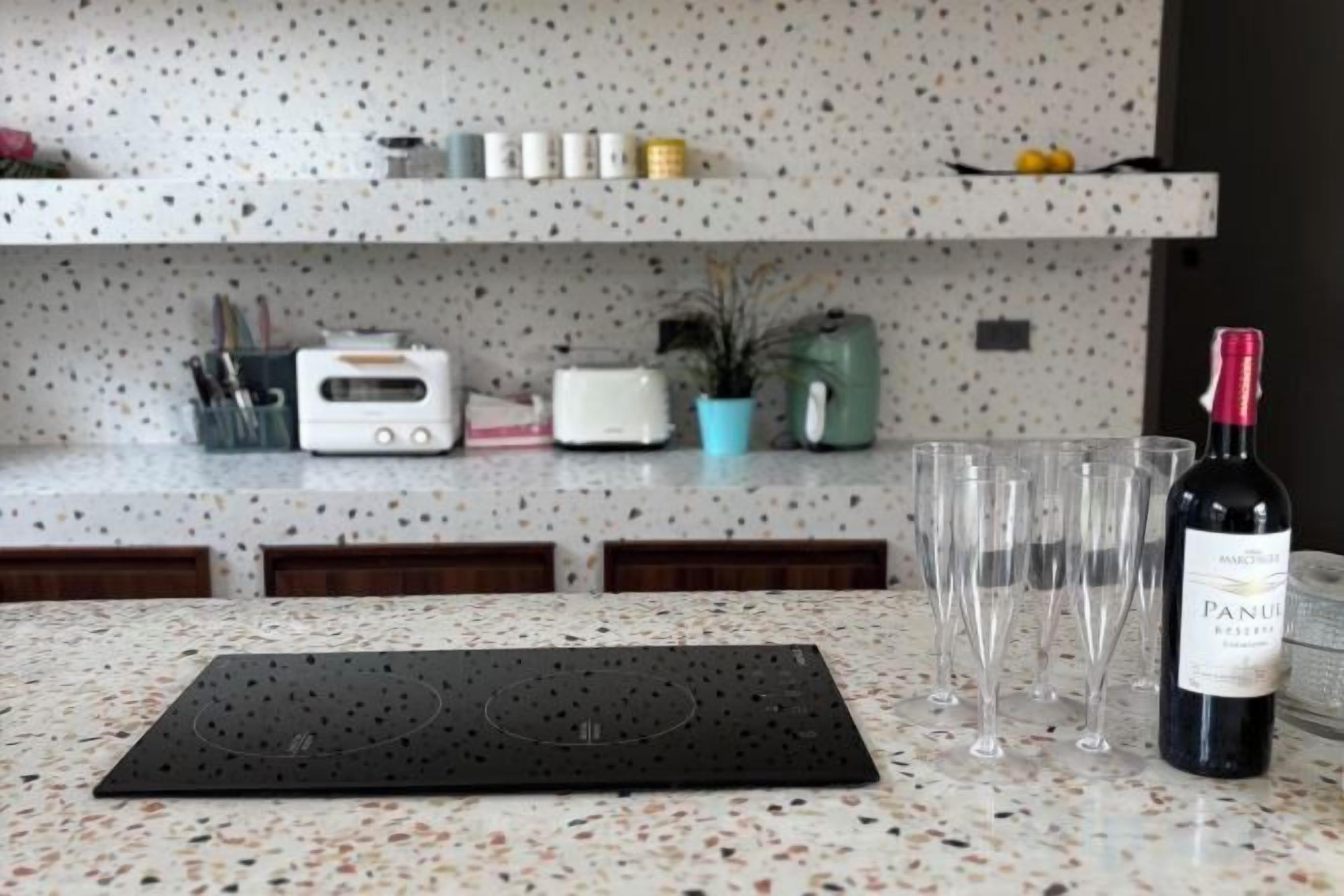 A kitchen counter with a wine bottle, glasses, a toaster, and a plant.