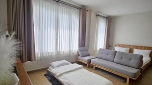 Ein Hotelzimmer mit einem Bett, einem grauen Sofa, einem Sessel und einem kleinen Tisch mit einer Vase weißer Blumen.