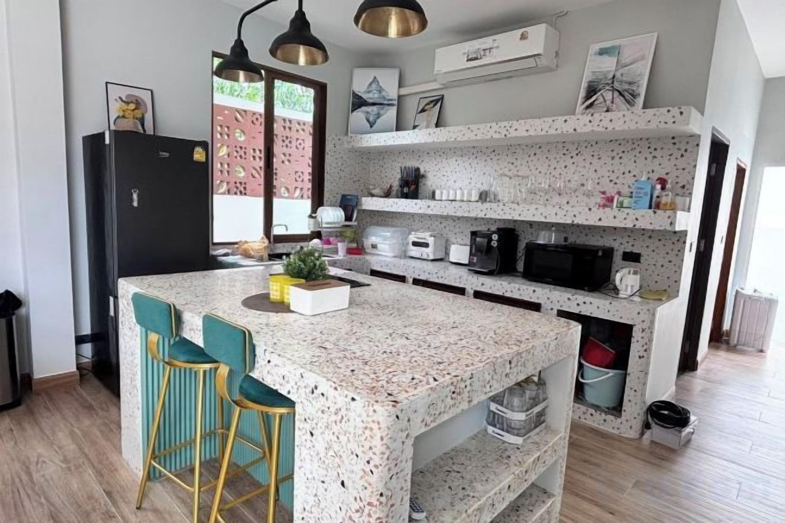 A kitchen with a speckled countertop, bar stools, a refrigerator, and a microwave.